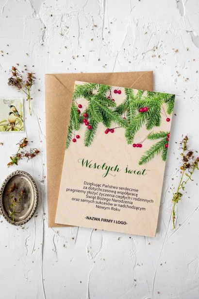 Drewniana kartka świąteczna z grafiką zielonych gałązek, personalizowana dla firm z ich logo i treścią życzeń.