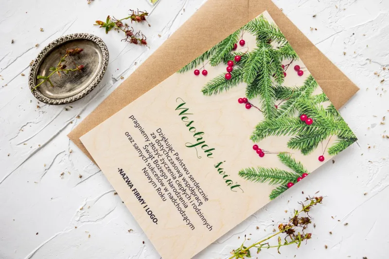 Drewniana kartka świąteczna z grafiką zielonych gałązek, personalizowana dla firm z ich logo i treścią życzeń.