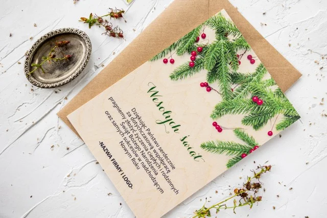 Drewniana kartka świąteczna z grafiką zielonych gałązek, personalizowana dla firm z ich logo i treścią życzeń.
