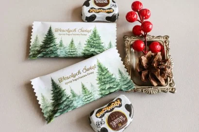 Personalizowane czekoladki świąteczne z logo firmy w białym opakowaniu z zielonymi choinkami.