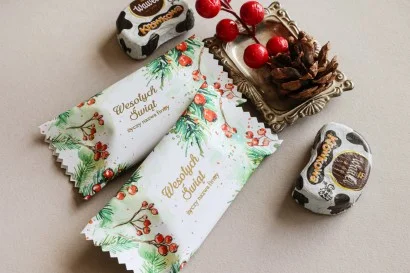 Personalizowane czekoladki świąteczne z logo firmy w eleganckim opakowaniu z zielonymi gałązkami i czerwonymi jagodami.