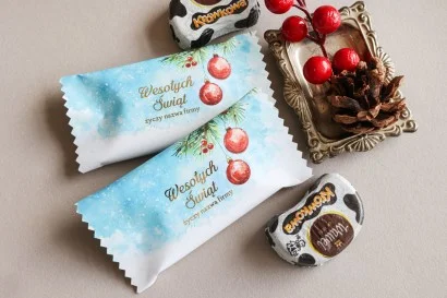Personalizowane czekoladki świąteczne z logo firmy w eleganckim niebiesko-białym opakowaniu z czerwonymi bombkami.