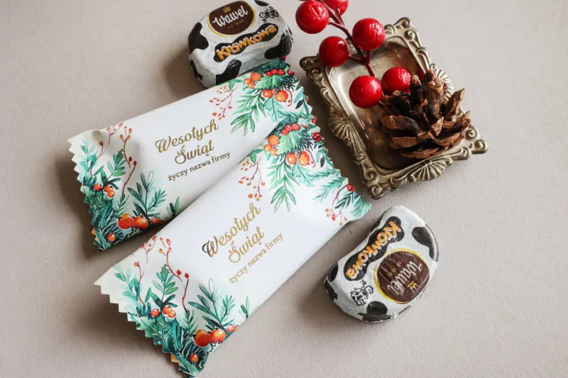 Czekoladki na Boże Narodzenie z grafiką zielonych liści i czerwonych jagód w białym opakowaniu. Czekoladki na Boże Narodzenie z grafiką zielonych liści i czerwonych jagód w białym opakowaniu.