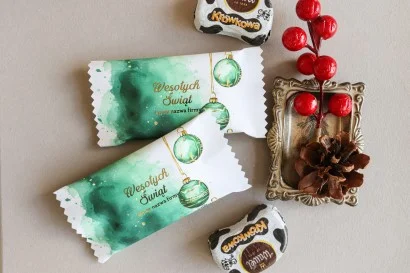 Personalizowane czekoladki świąteczne z logo firmy w eleganckim białym opakowaniu z zielonymi bombkami.