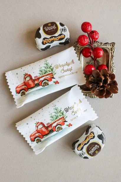 Personalizowane czekoladki świąteczne z logo firmy w eleganckim opakowaniu z grafiką czerwonej ciężarówki przewożącej choinkę.