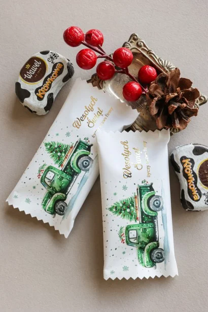 Personalizowane czekoladki świąteczne z logo firmy w eleganckim opakowaniu z grafiką zielonej ciężarówki przewożącej choinkę.