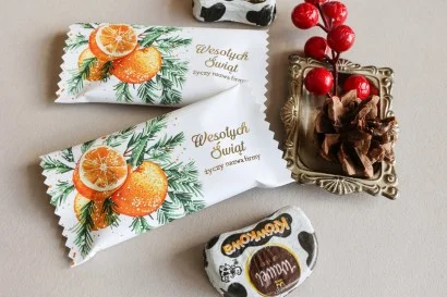 Personalizowane czekoladki świąteczne z logo firmy w eleganckim białym opakowaniu z grafiką pomarańczy i gałązek jodły.