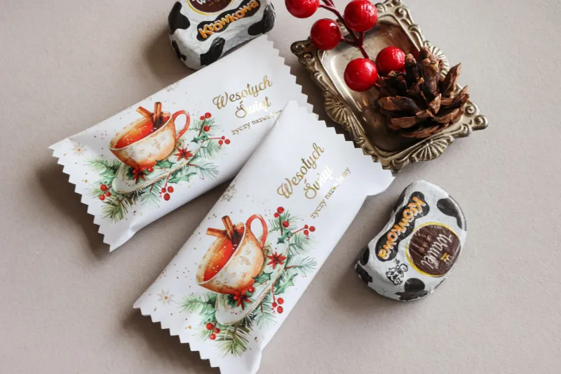 Świąteczne czekoladki w białym opakowaniu z grafiką filiżanki z cynamonem, gałązkami jodły i czerwonymi owocami ostrokrzewu. Świąteczne czekoladki w białym opakowaniu z grafiką filiżanki z cynamonem, gałązkami jodły i czerwonymi owocami ostrokrzewu.