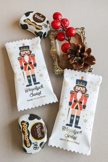 Eleganckie czekoladki świąteczne w białym opakowaniu z grafiką żołnierza w czerwonym stroju, idealne na prezenty firmowe.
