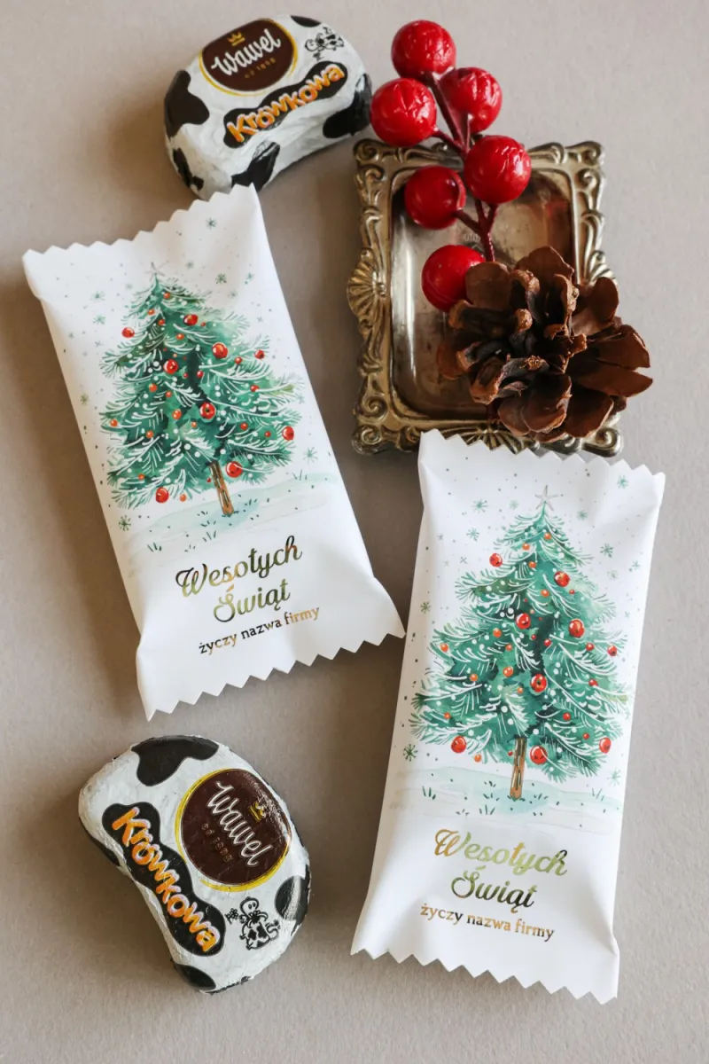 Świąteczne czekoladki w białym opakowaniu z grafiką choinki, udekorowanej czerwonymi bombkami i światełkami. Świąteczne czekoladki w białym opakowaniu z grafiką choinki, udekorowanej czerwonymi bombkami i światełkami.