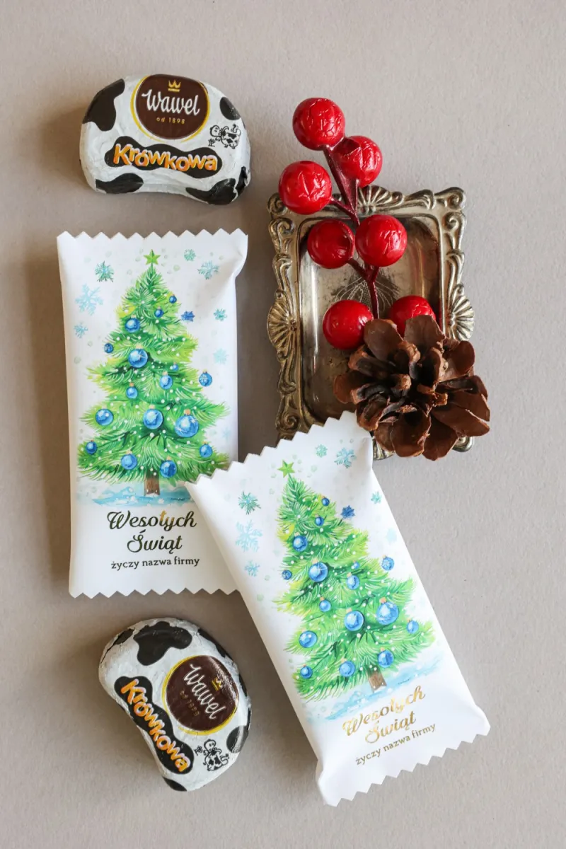 Świąteczne czekoladki w białym opakowaniu z grafiką choinki udekorowanej niebieskimi bombkami i światełkami. Świąteczne czekoladki w białym opakowaniu z grafiką choinki udekorowanej niebieskimi bombkami i światełkami.