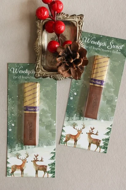 Firmowe czekoladki Merci z akwarelową grafiką zimowego krajobrazu i śnieżnymi choinkami, idealne na świąteczne upominki.